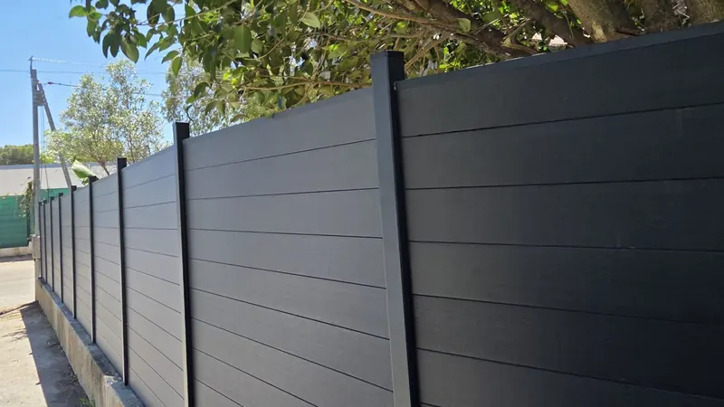 Clôture en lames composite anthracite et poteaux aluminium noirs posée sur un muret existant, vue en enfilade