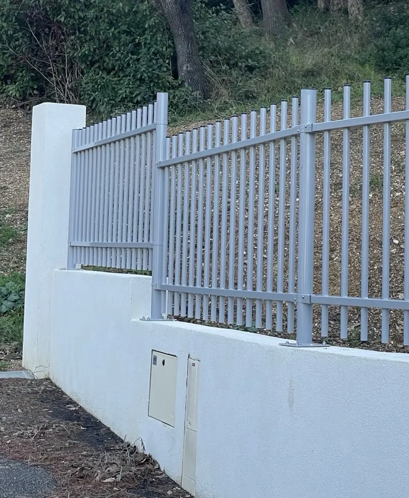 Muret enduit blanc avec pilier et coffrets techniques intégrés, surmonté d'une clôture à barreaudage aluminium