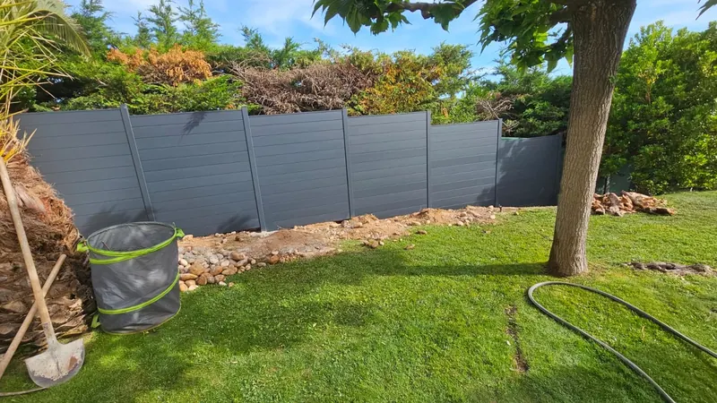 Clôture en lames aluminium gris anthracite posée en pleine terre, en redans, dans un jardin en pente