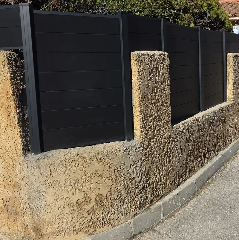 Lames composite anthracite posées entre les piliers crépis d'un muret arrondi, en bordure de rue