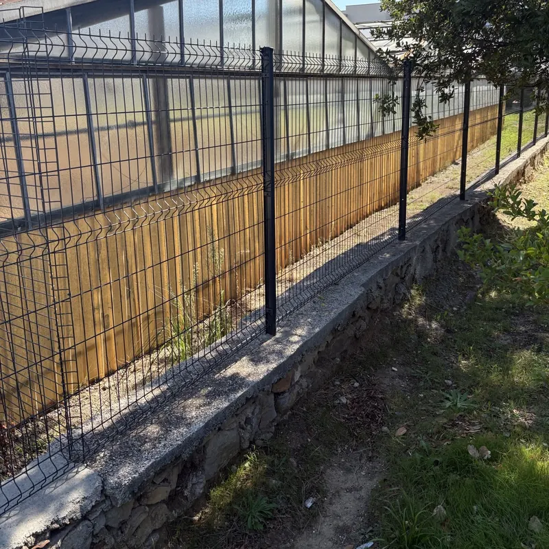 Grillage rigide anthracite posé sur un muret en pierres existant, poteaux scellés dans son chaperon béton