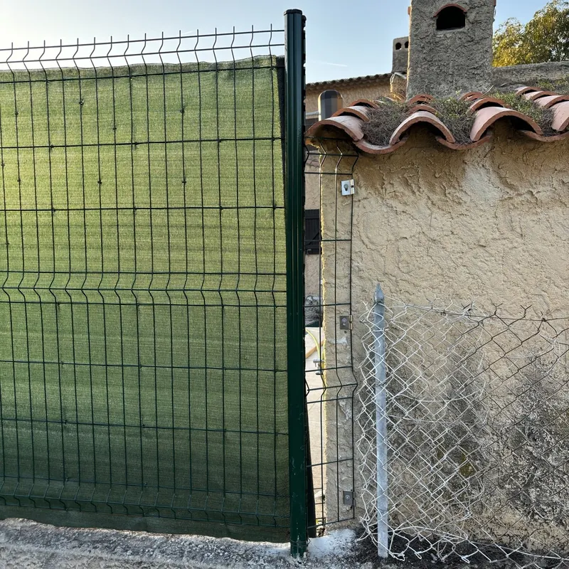 Toile brise-vue verte fixée sur un panneau de grillage rigide vert, panneau recoupé fixé au mur par platines