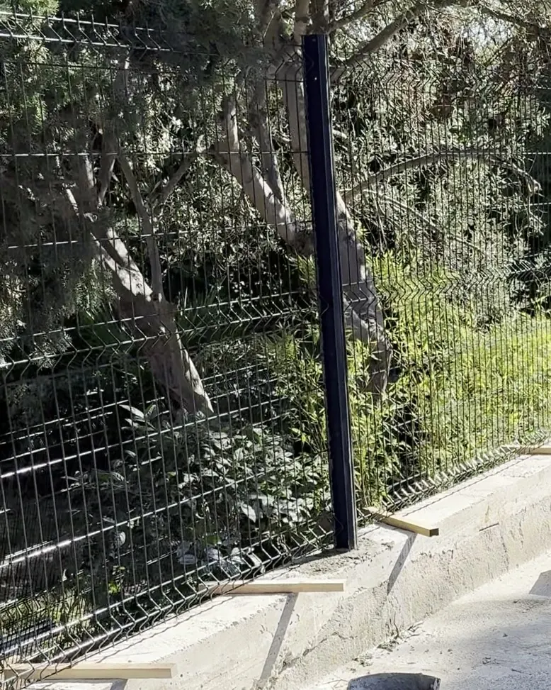 Panneaux de grillage rigide anthracite calés sur tasseaux au-dessus d'une longrine béton, pendant la pose